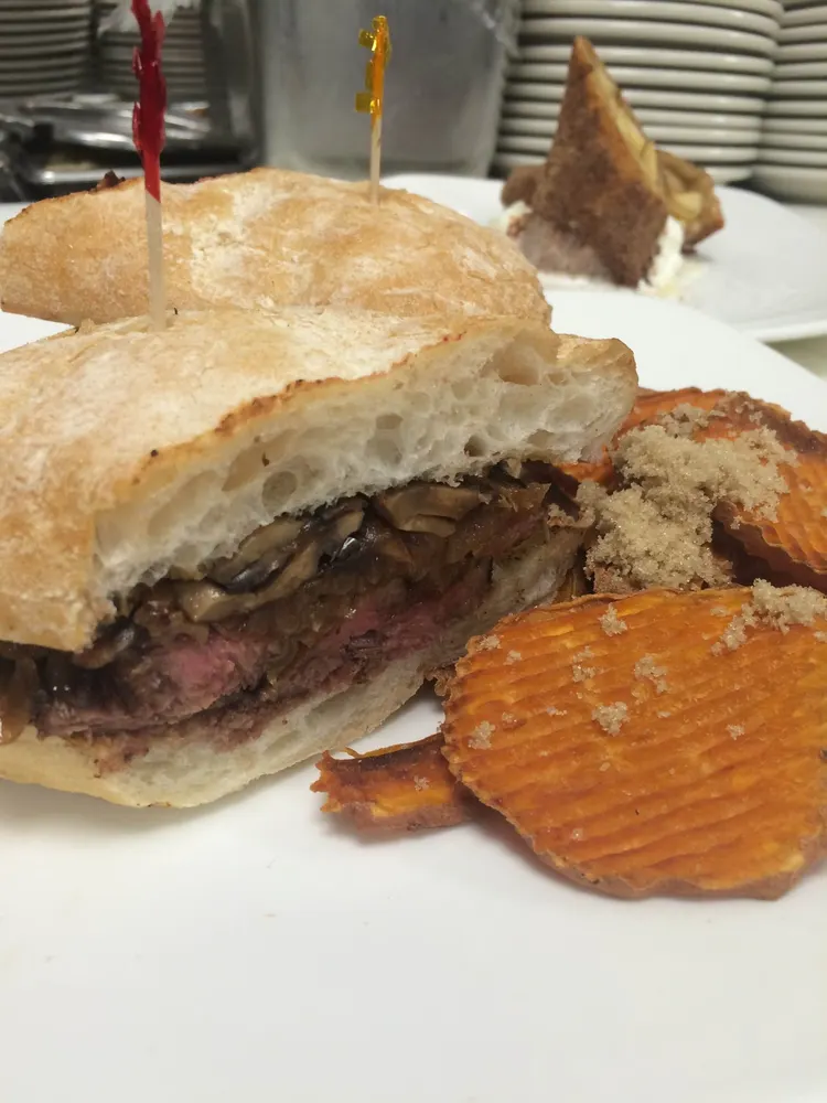 A steak sandwich on a crusty roll with sweet potato chips